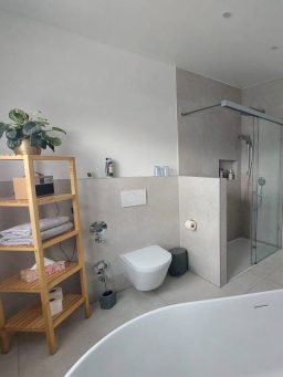 Modernes Badezimmer mit Dusche, WC, Regalkonstruktion und Pflanzen.