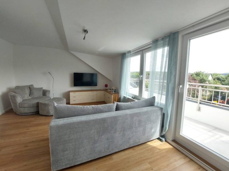 Stilvolles Wohnzimmer mit grauem Sofa, Fernseher und Blick auf den Balkon.