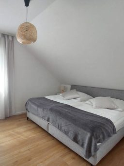 Schlafzimmer mit einem Doppelbett, grauer Bettdecke und einer Pendelleuchte.