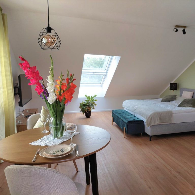 Helles, modernes Zimmer mit Blumenarrangement, Bett und Essbereich.